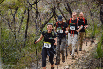 Image of an Oxfam Trailwalker team on a bush trail in single file all using trekking poles.